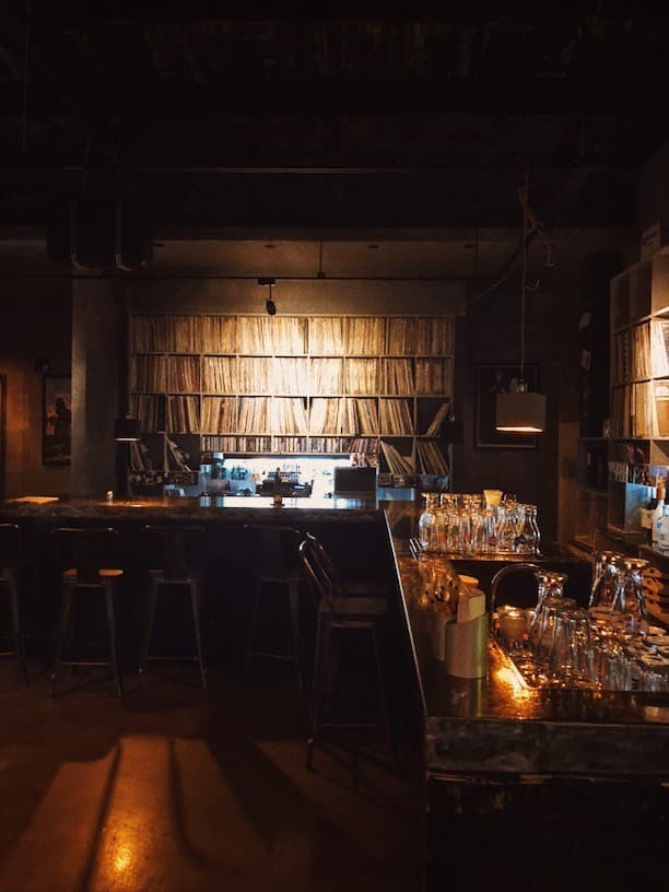 충청북도 충주시 벙커 LP Bar - 벽면 가득한 LP 레코드와 낮은 조명이 비추는 다찌석. 혼술을 위한 바 테이블 위 투명한 유리잔들이 정렬된 LP바 내부