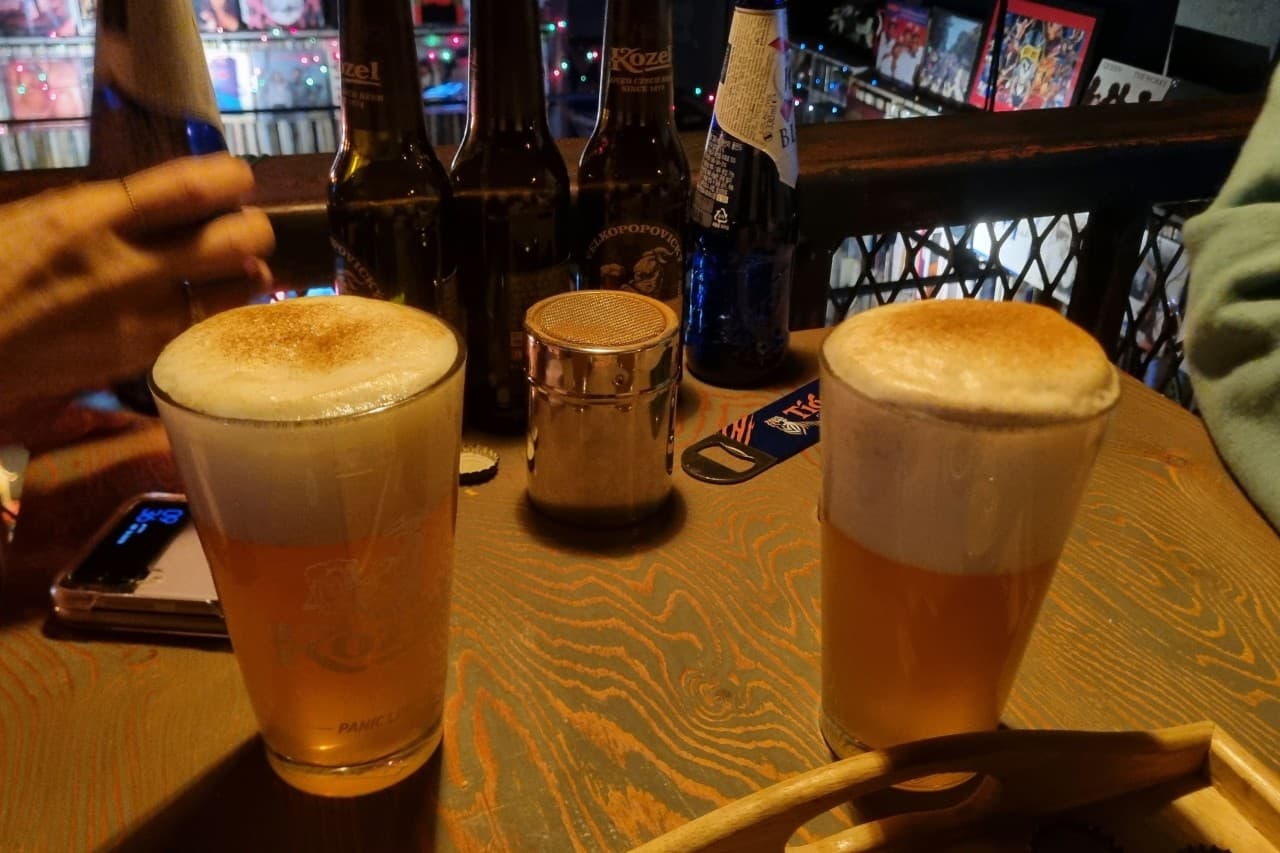 충청북도 충주시 벙커 LP Bar - LP바 다찌석에 놓인 시나몬 가루 얹은 맥주와 병맥주. 배경의 LP판 진열장과 조명이 비치는 1인 혼술 상황.