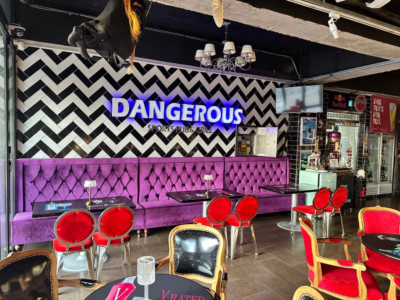 충청북도 충주시 DANGEROUS PUB 바 내부. 파란 네온사인과 지그재그 벽면 아래 보라색 벨벳 소파와 빨간 의자가 배치된 1인석 테이블에서 혼술을 즐기는 상황.