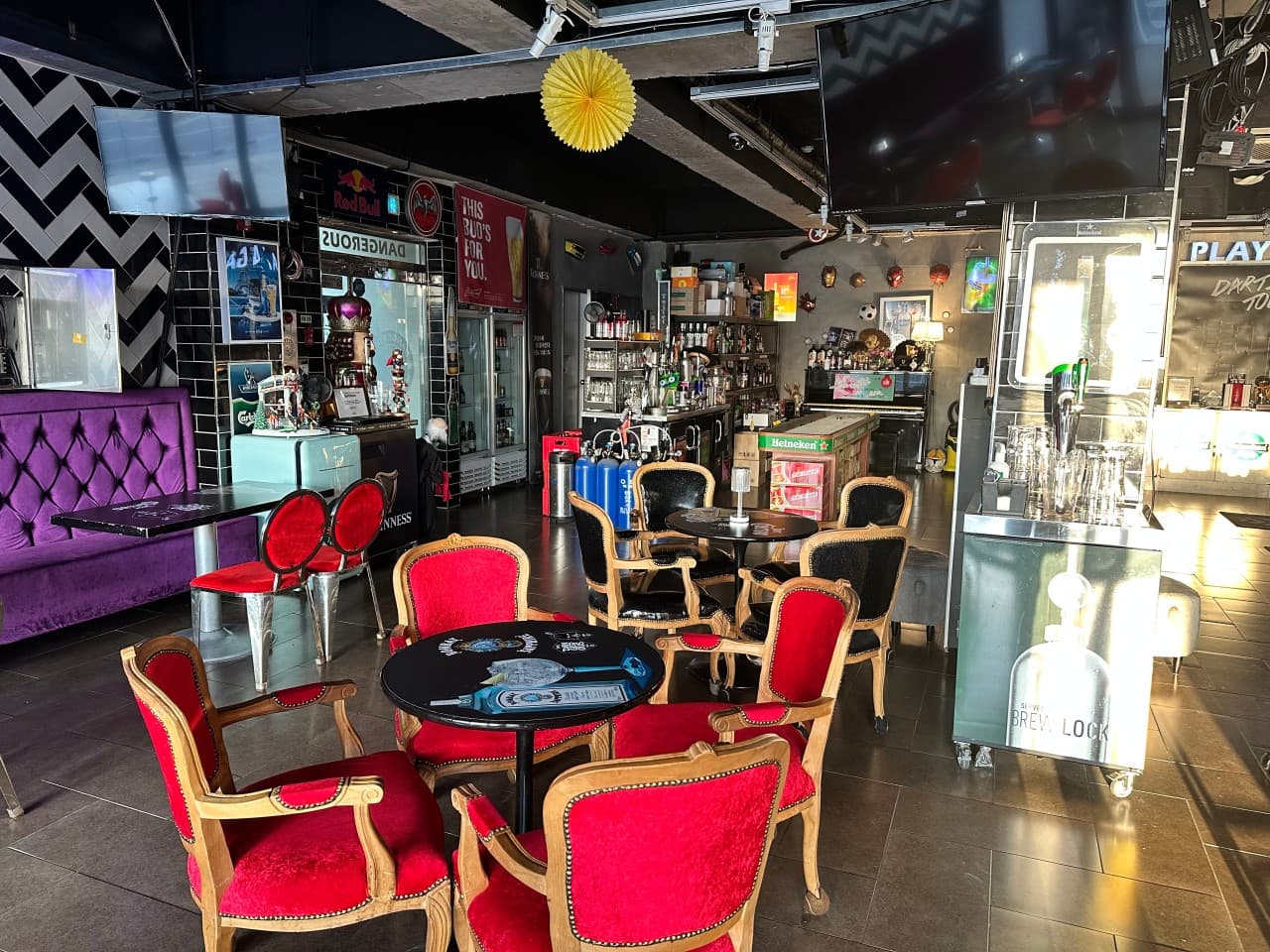 충청북도 충주시 DANGEROUS PUB 바의 빨간 벨벳 의자와 보라색 소파 좌석. 지그재그 패턴 벽면과 혼술 가능한 바 카운터, 밝은 조명 아래 배치된 원형 테이블과 주류병들.