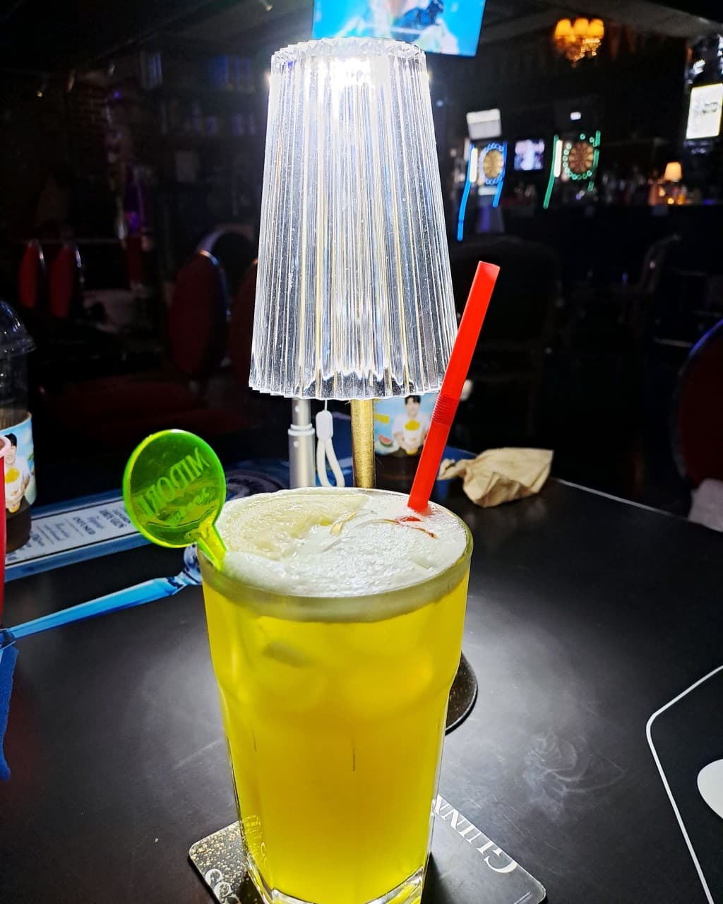 충청북도 충주시 혼술 바 DANGEROUS PUB - 테이블 조명 아래 거품 얹은 노란색 칵테일과 다트 머신이 보이는 어두운 실내 1인석