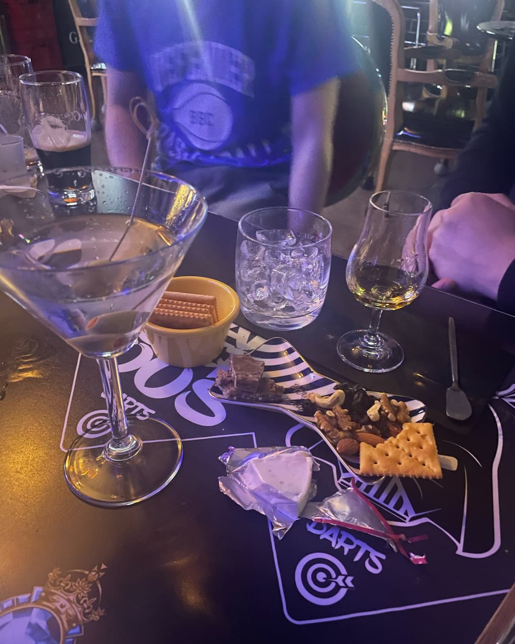 충청북도 충주시 DANGEROUS PUB 바(Bar)의 어두운 조명 아래 올리브 마티니와 위스키, 견과류와 치즈 안주가 차려진 테이블. 다찌석에서 혼술을 하는 상황.
