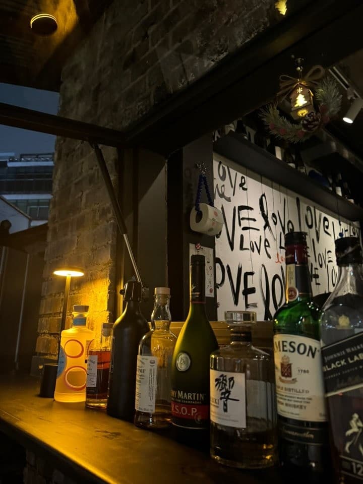 충청북도 충주시 혼술 바(Bar) 뚤리 다찌석에 놓인 위스키 병들과 노란 조명. LOVE 낙서가 있는 벽면 배경으로 어두운 실내에서 즐기는 1인 술자리.