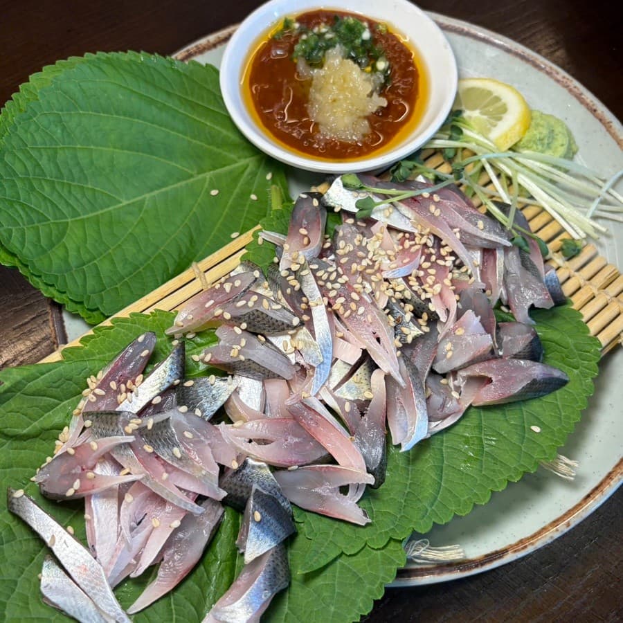 충청북도 청주시 요리주점 회오리 청주율량점의 혼술 메뉴. 깻잎과 대나무 발 위 전어회와 다진 마늘 양념장. 다찌석 조명 아래 생선 질감과 레몬, 와사비가 차려진 1인 상차림.