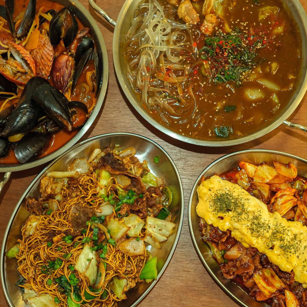 충청북도 청주시 무아지경 요리주점 - 노란 조명 아래 해물찜, 당면 찜닭, 볶음면이 차려진 1인 다찌석 혼술 상차림