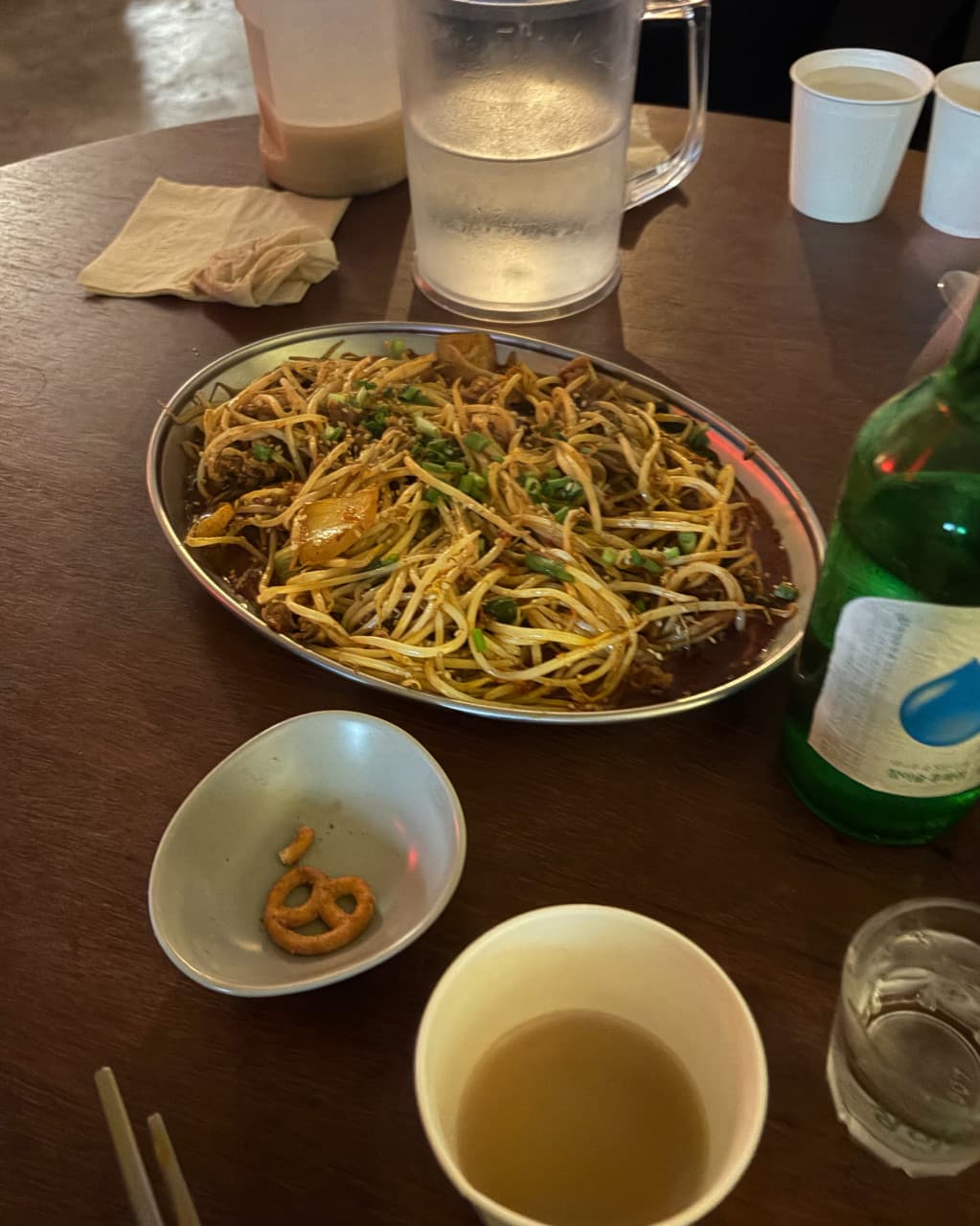 충청북도 청주시 요리주점 무아지경 - 노란 조명 아래 나무 테이블 위 숙주 볶음과 소주 한 병. 1인 혼술 상황의 프레첼과 종이컵이 놓인 다찌석 분위기.