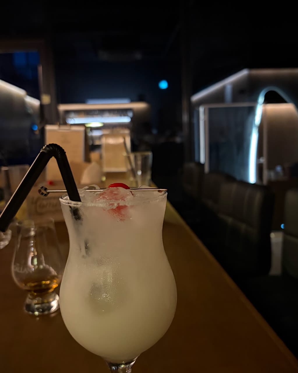 충청남도 천안시 혼술바 고도 불당점 바(Bar) - 어두운 조명 아래 다찌석에 놓인 흰색 칵테일의 차가운 질감과 1인 좌석에서 즐기는 정적인 분위기