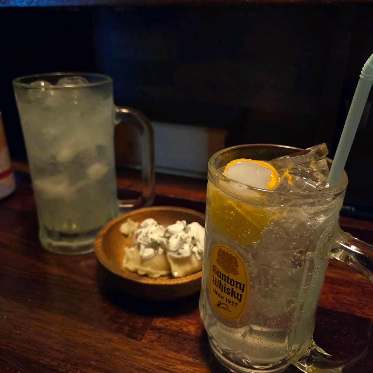충청남도 천안시 요리주점 오늘도 천안두정의 어두운 나무 다찌석. 레몬 조각을 띄운 하이볼과 하얀 소스가 얹어진 안주가 조명을 받으며 혼술 분위기를 조성한다.