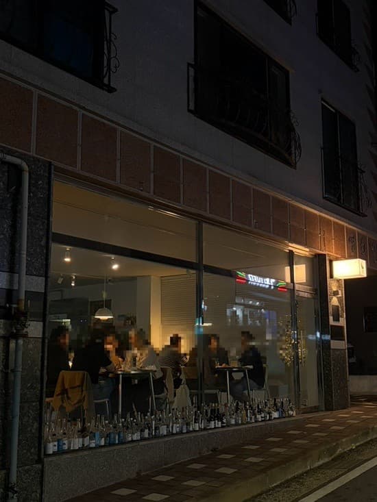 충청남도 천안시 요리주점 은월주. 밤 시간 통창 너머 노란 조명이 켜진 내부와 혼술 가능한 다찌석. 창가 아래 일렬로 늘어선 빈 술병들이 보이는 건물 외관.